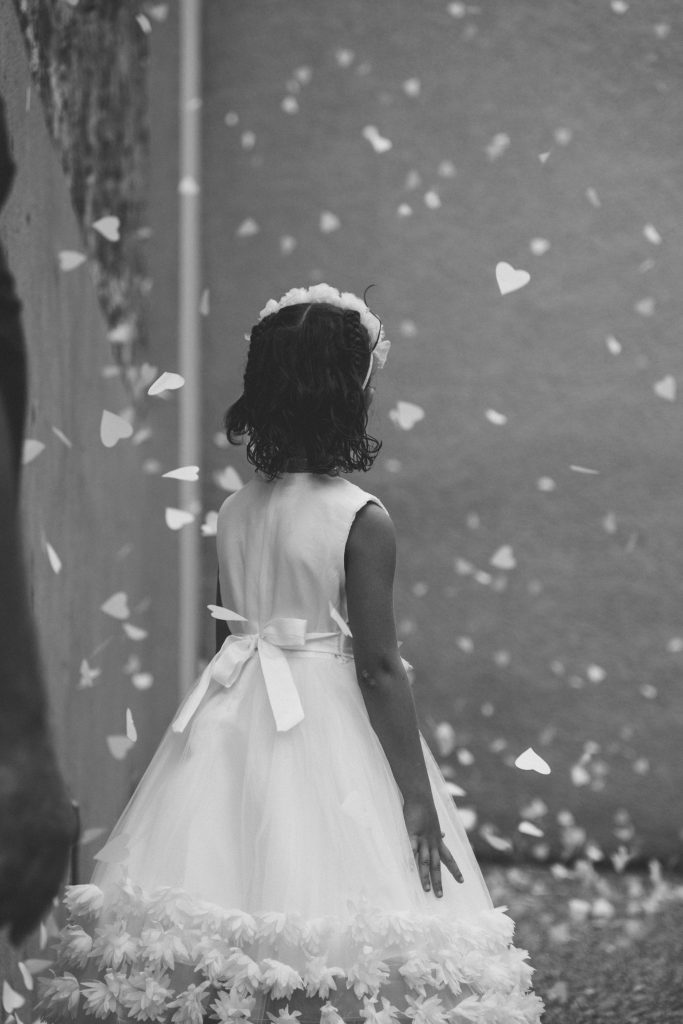 Petite fille de dos en robe blanche lors d’un mariage en Haute-Loire, entourée de confettis colorés qui volent dans l’air. Moment magique et joyeux capturé par un photographe de mariage professionnel.